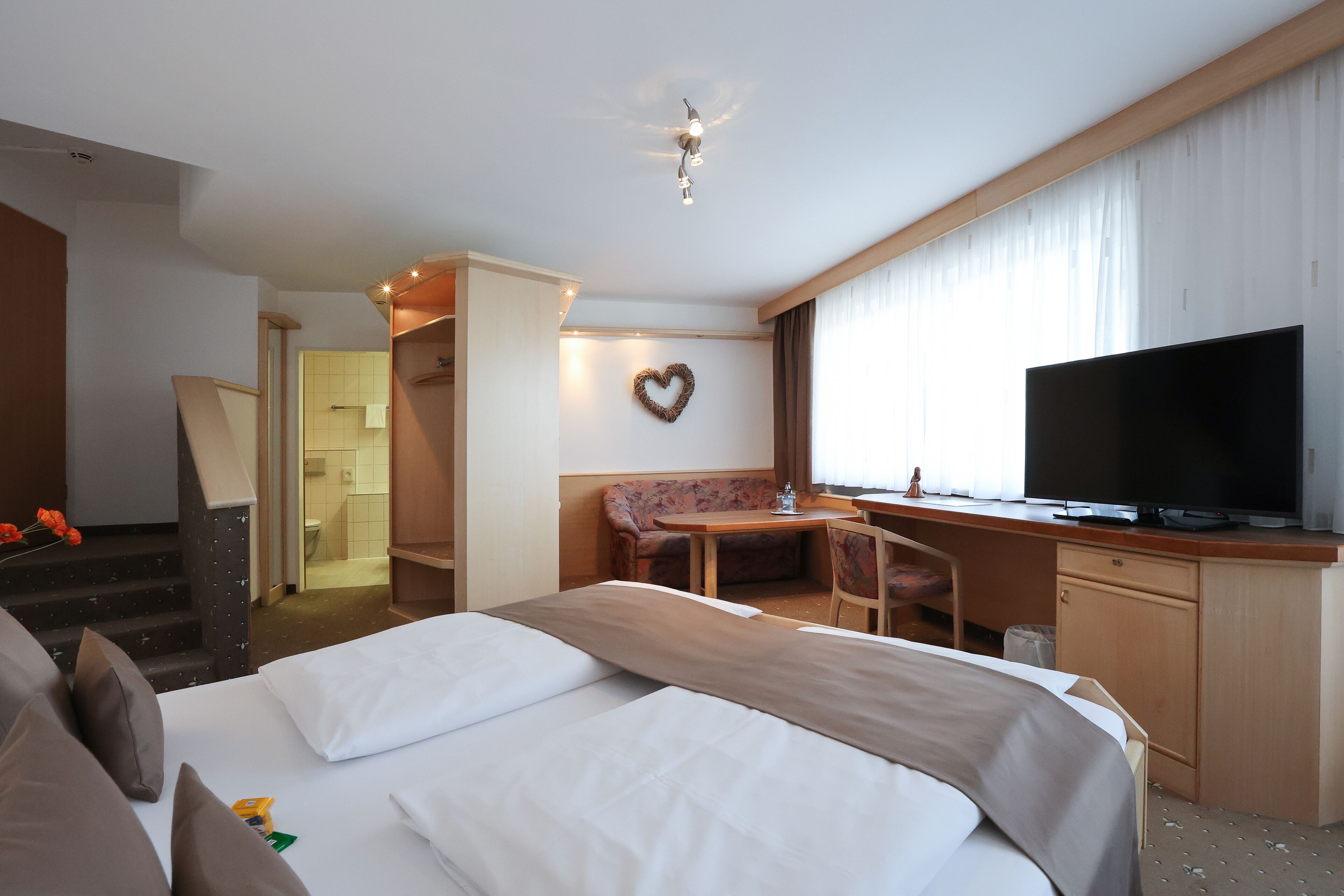 A hotel room with a bed, a desk, a television, and a heart-shaped decoration on the wall.