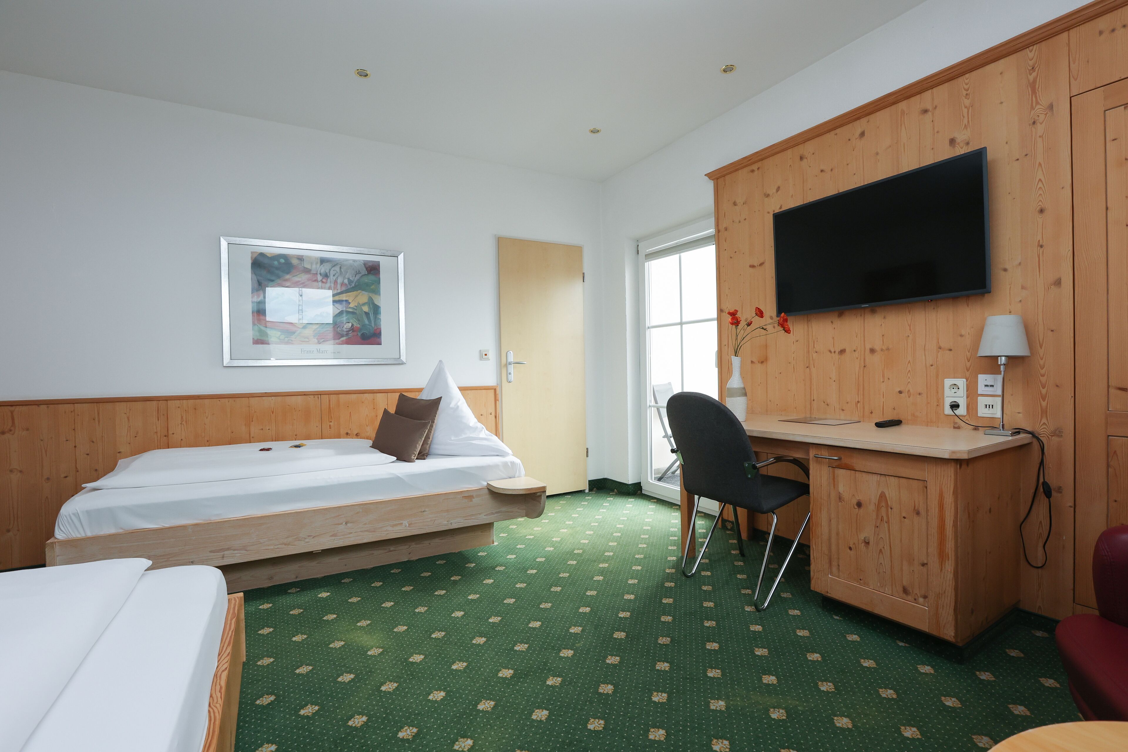A hotel room with two single beds, a desk with a chair, a television, and a framed picture on the wall.