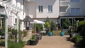 A courtyard with a paved walkway, outdoor seating, and potted plants. - Arthotel ANA Panorama, Trademark Collection by Wyndham (Marktoberdorf)