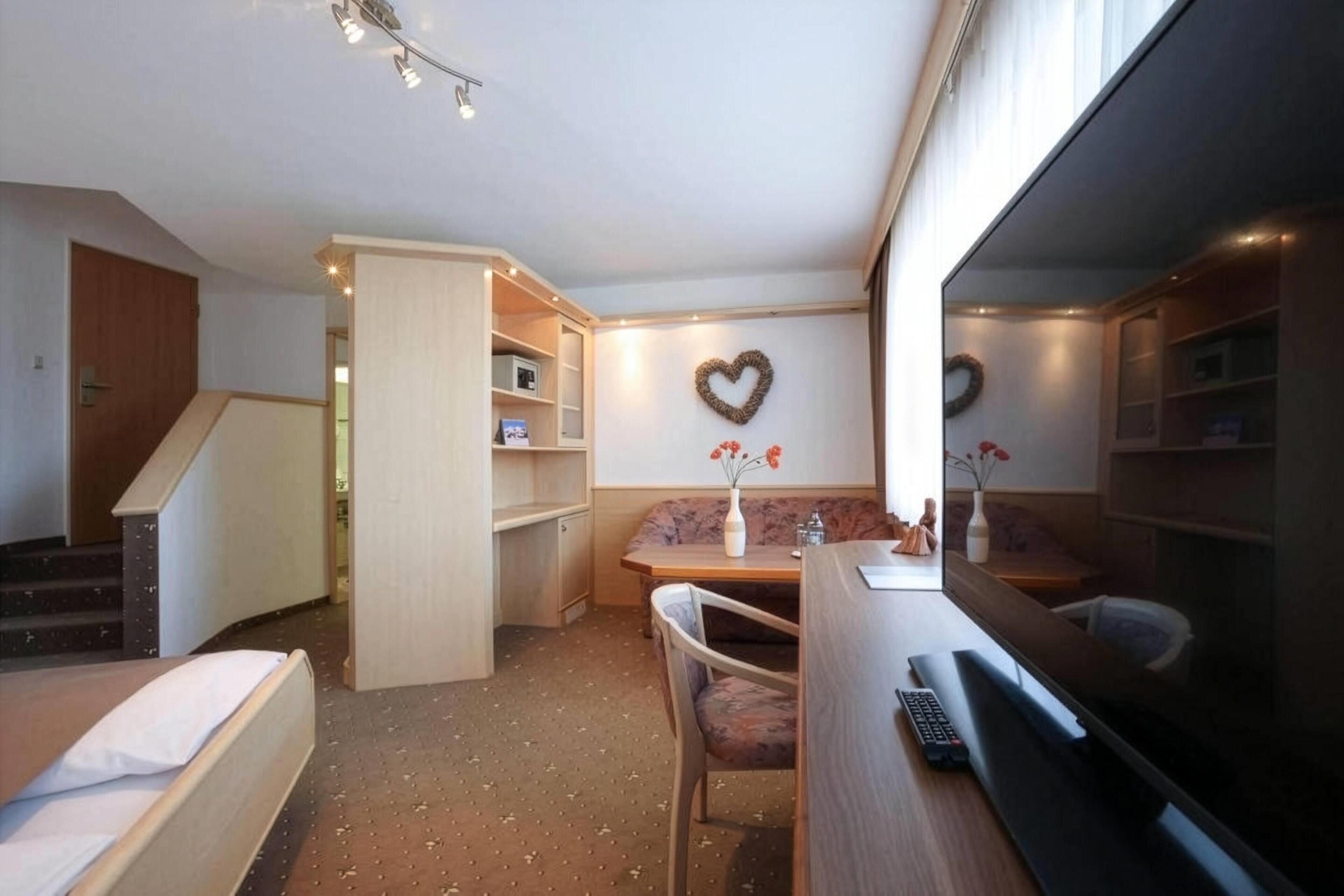 A compact hotel room with a bed, a desk, a chair, a small table, a sofa, and a TV.