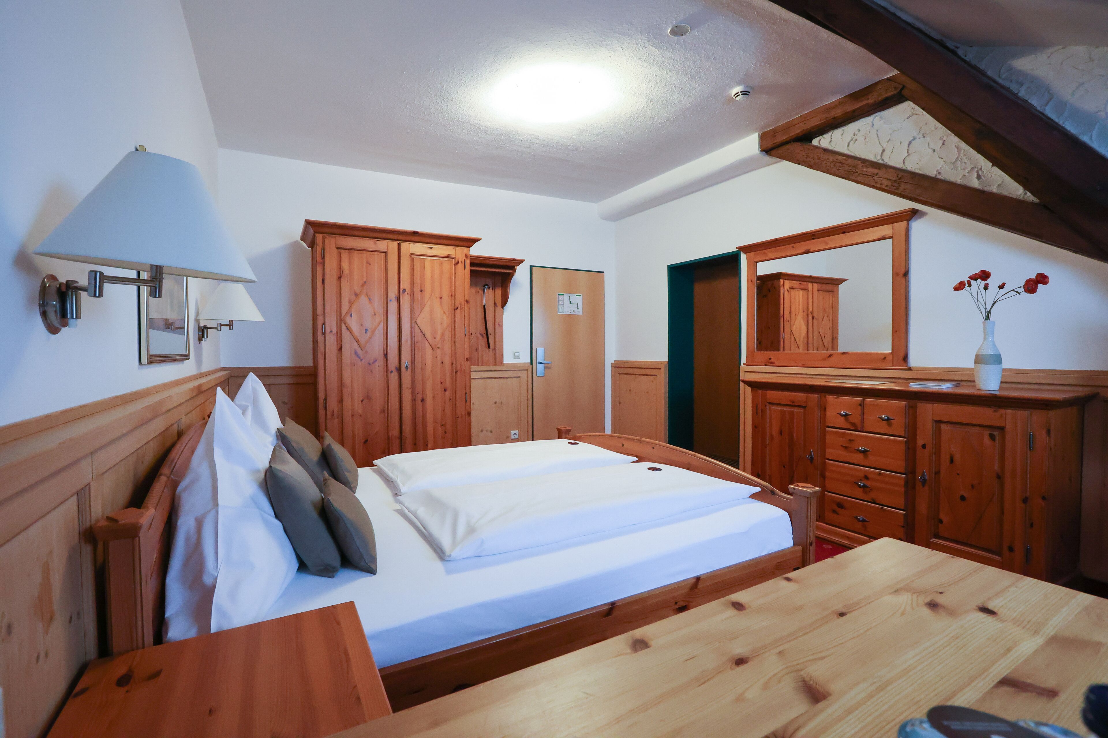Un dormitorio de madera con cama, cómoda, espejo y lámpara.