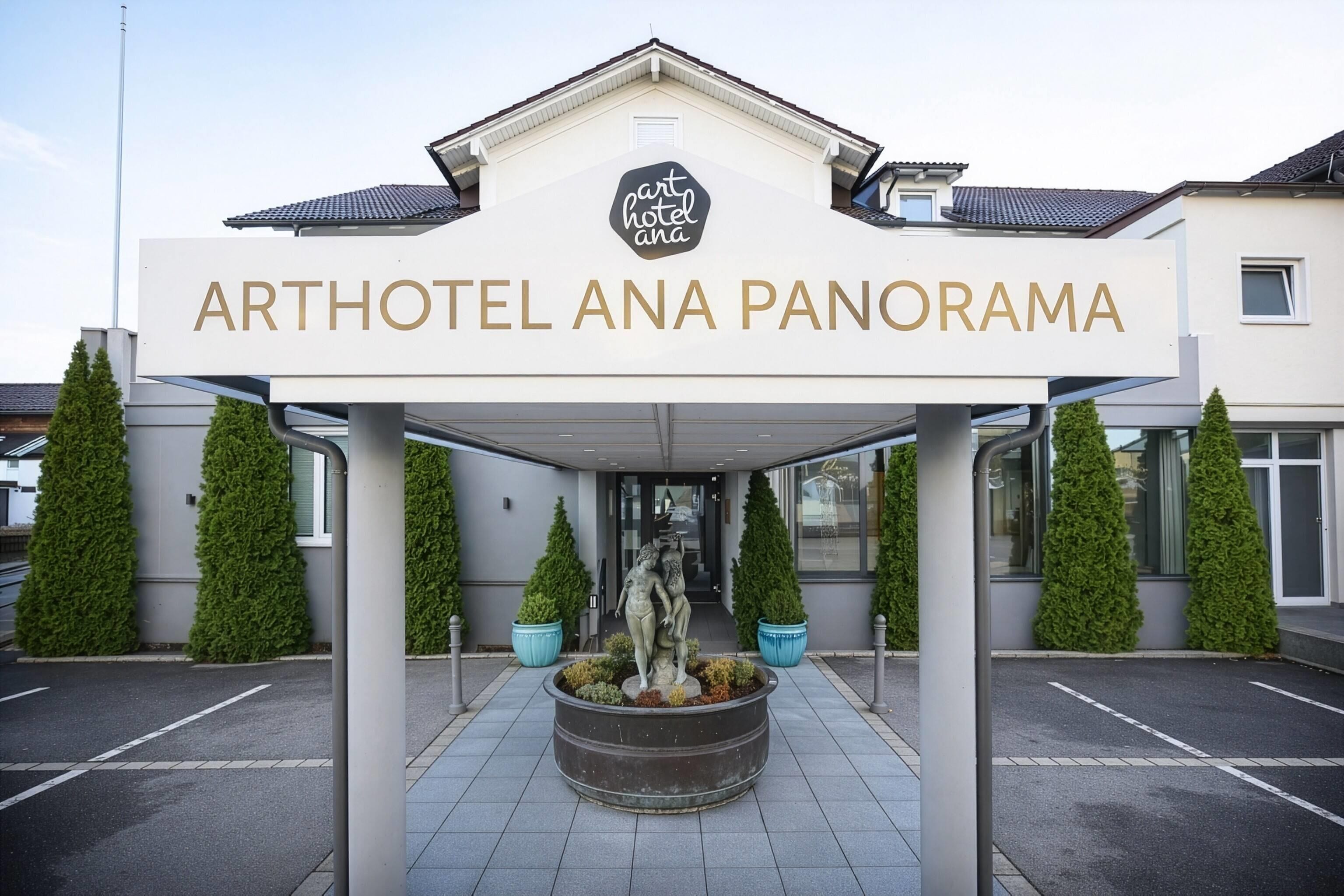 Der Eingang des Arthotel Ana Panorama mit freiem Blick auf die Fassade des Gebäudes, eine zentrale Statue und symmetrisch gestaltete Grünflächen.