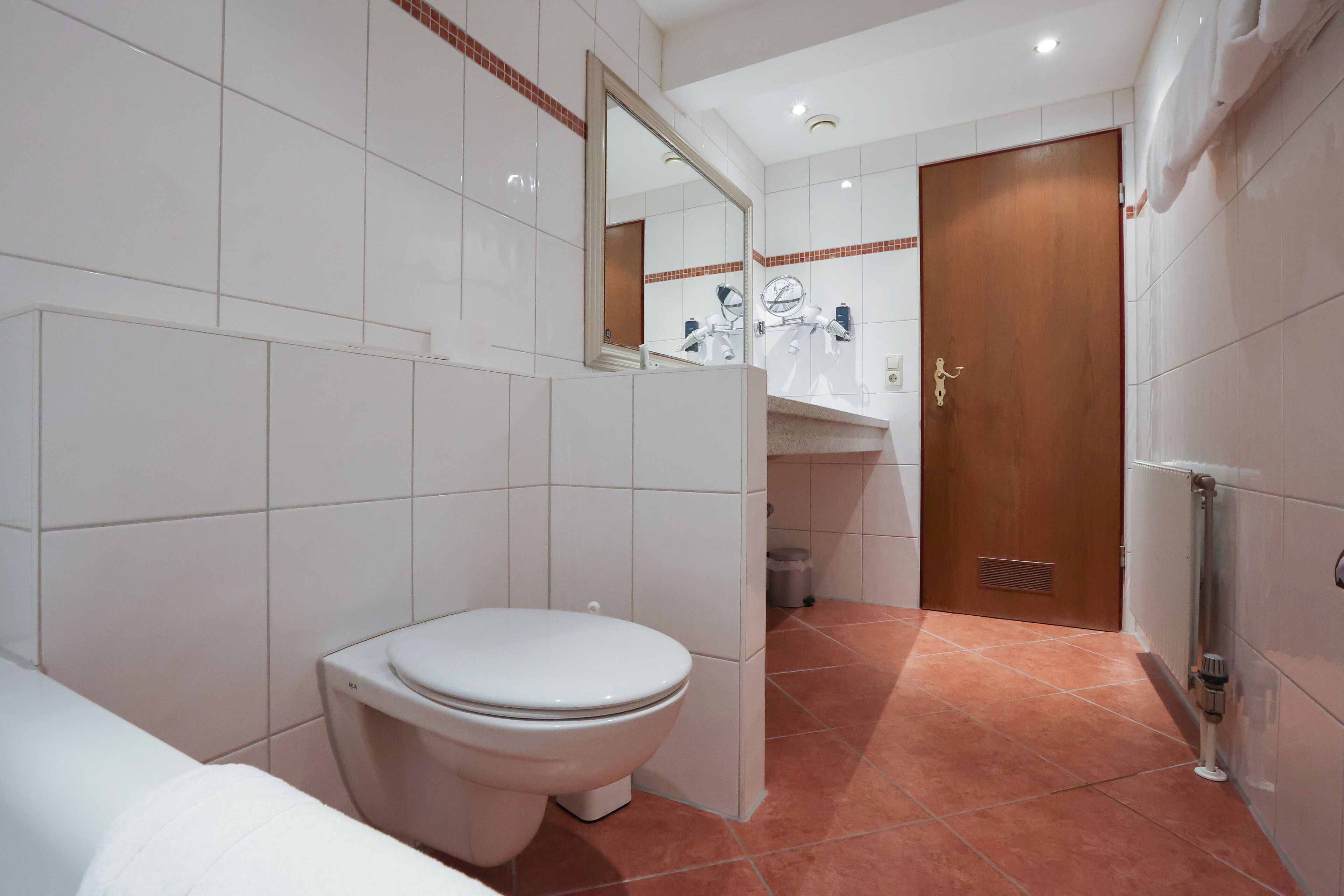 A modern bathroom with a white toilet, a sink with a mirror, and a shower area.