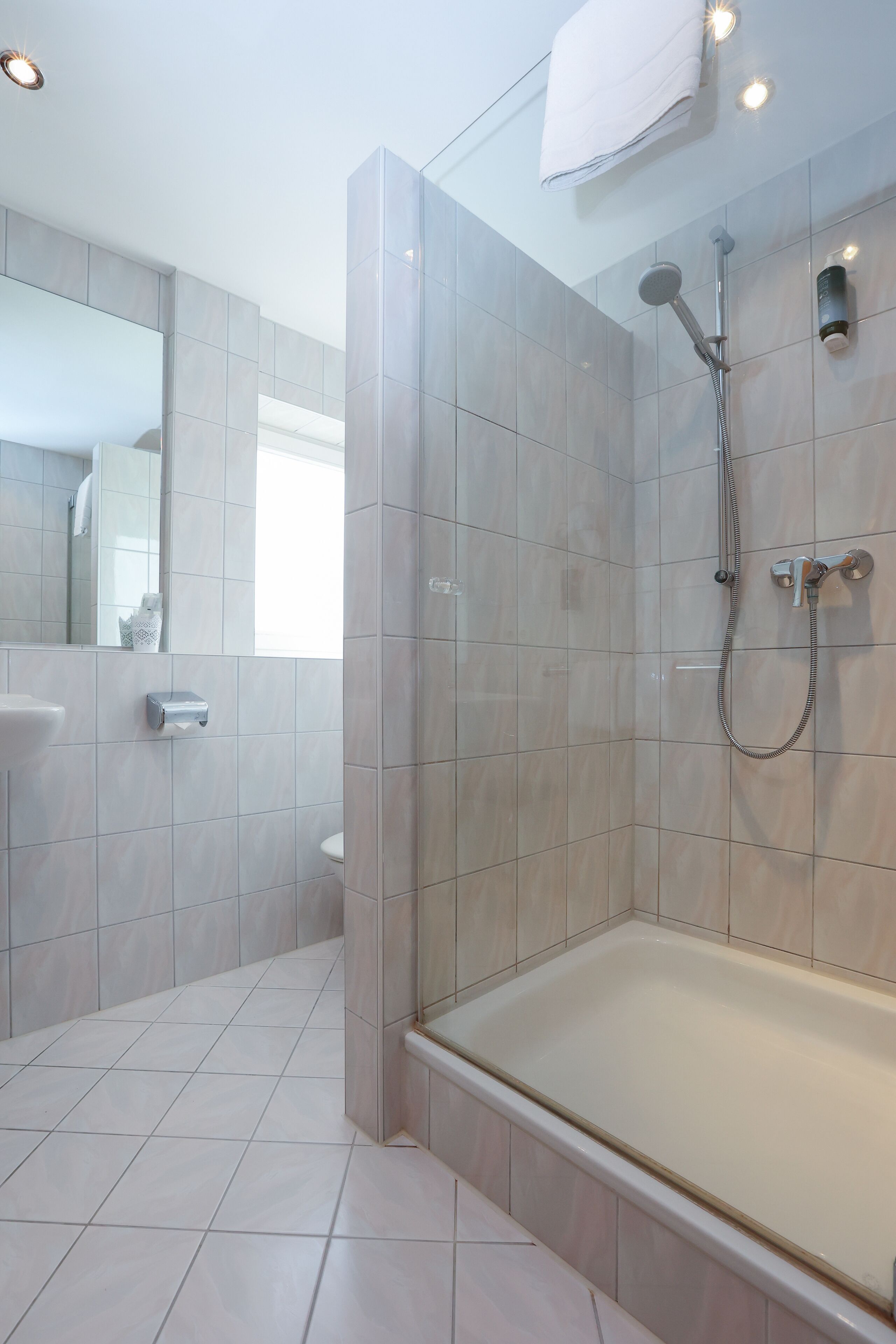 Un baño moderno con ducha de vidrio, bañera blanca y espejo grande.