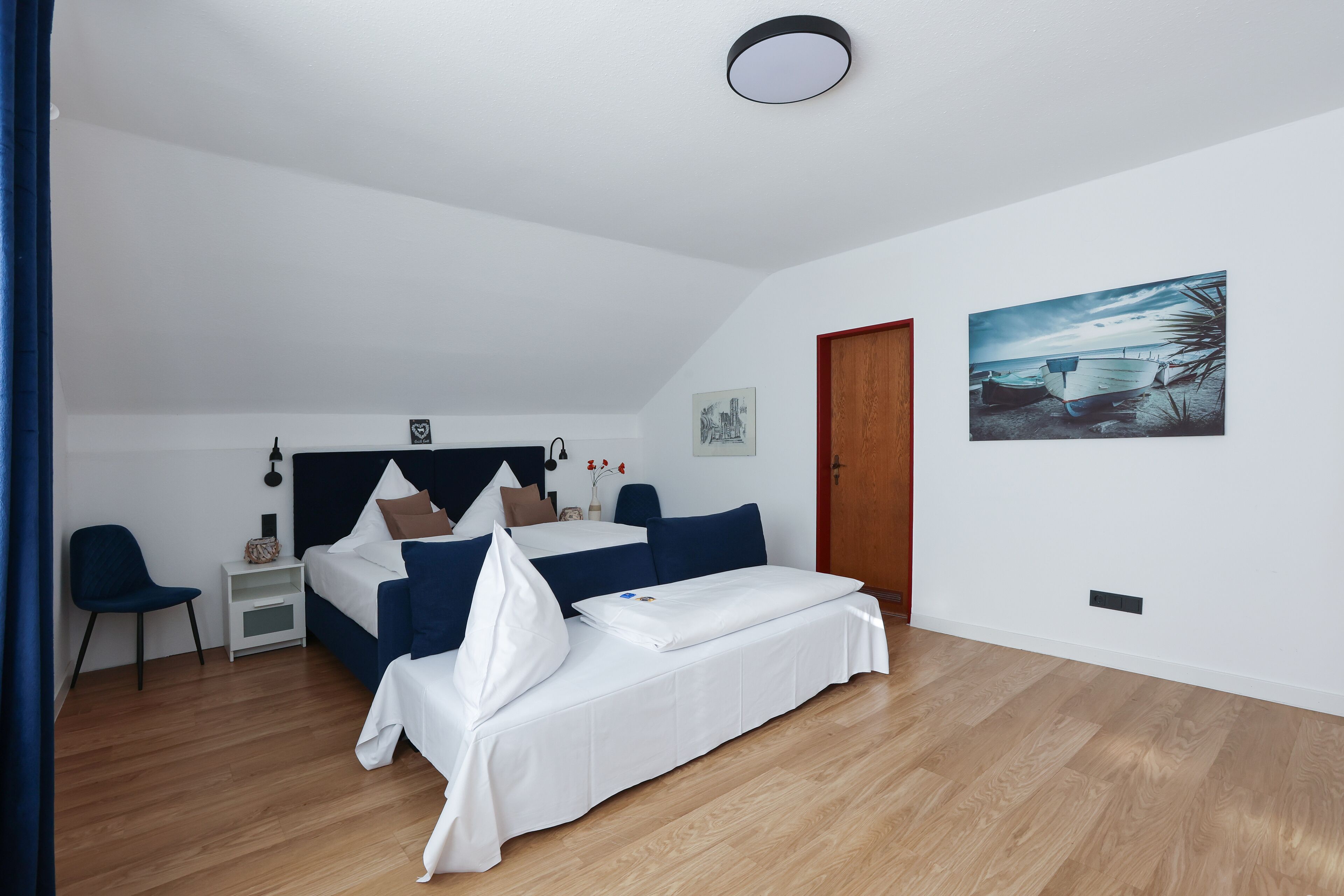 A bedroom with a bed, bedside table, chair, and artwork on the wall.