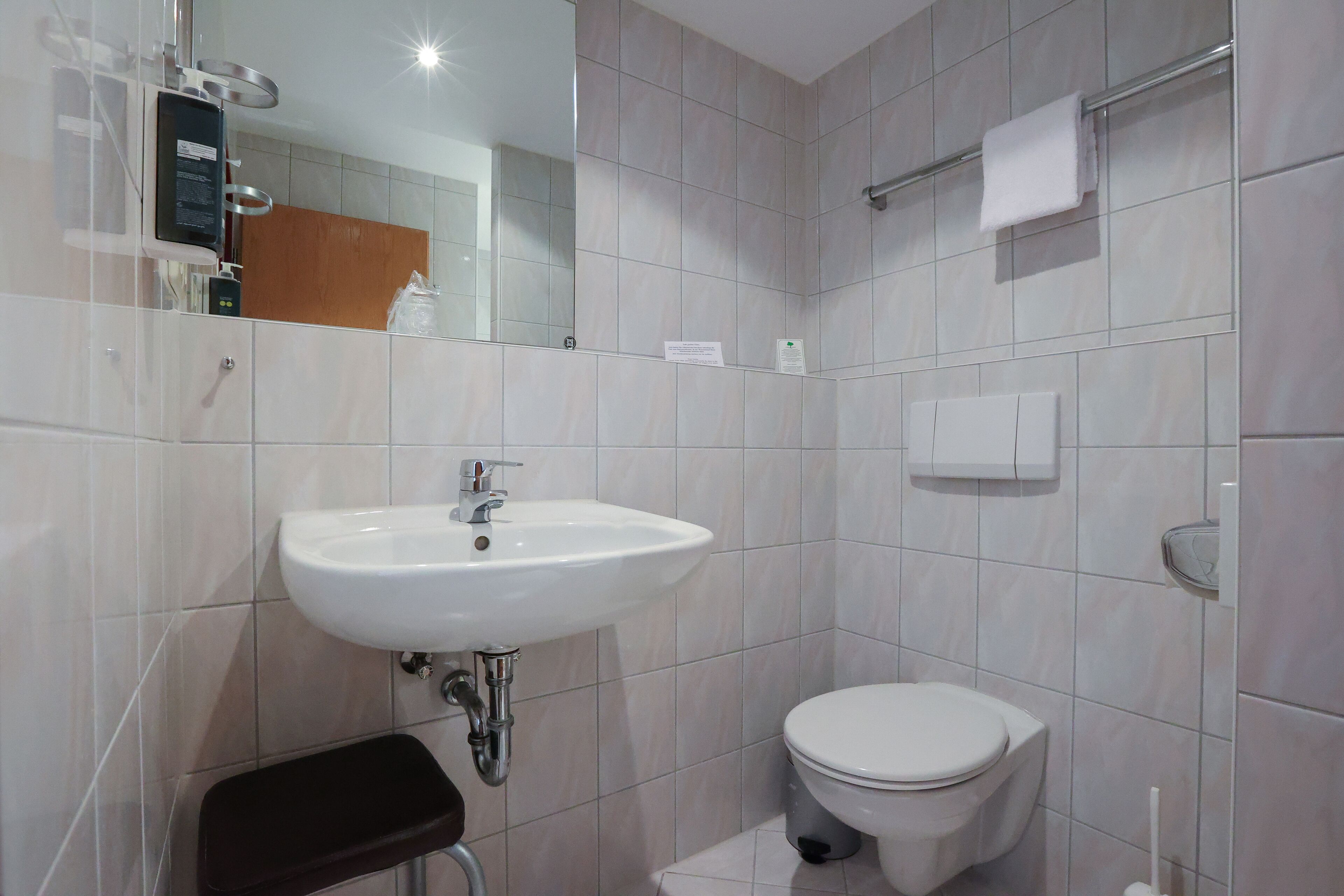 A modern bathroom with a white sink, toilet, and a small step stool.