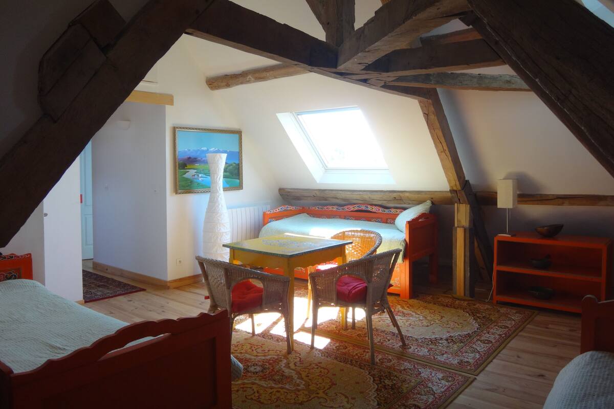 Une chambre mansardée avec un plafond en pente, une lucarne, un lit, une table et une chaise.
