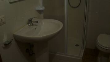 Une salle de bain avec un lavabo blanc, un miroir, des toilettes et un espace douche.