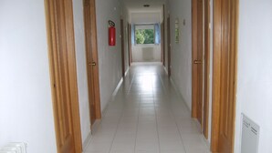 Ein langer, schmaler Korridor mit Holztüren an beiden Seiten, einem weißen Fliesenboden und einem an der Wand befestigten Feuerlöscher.