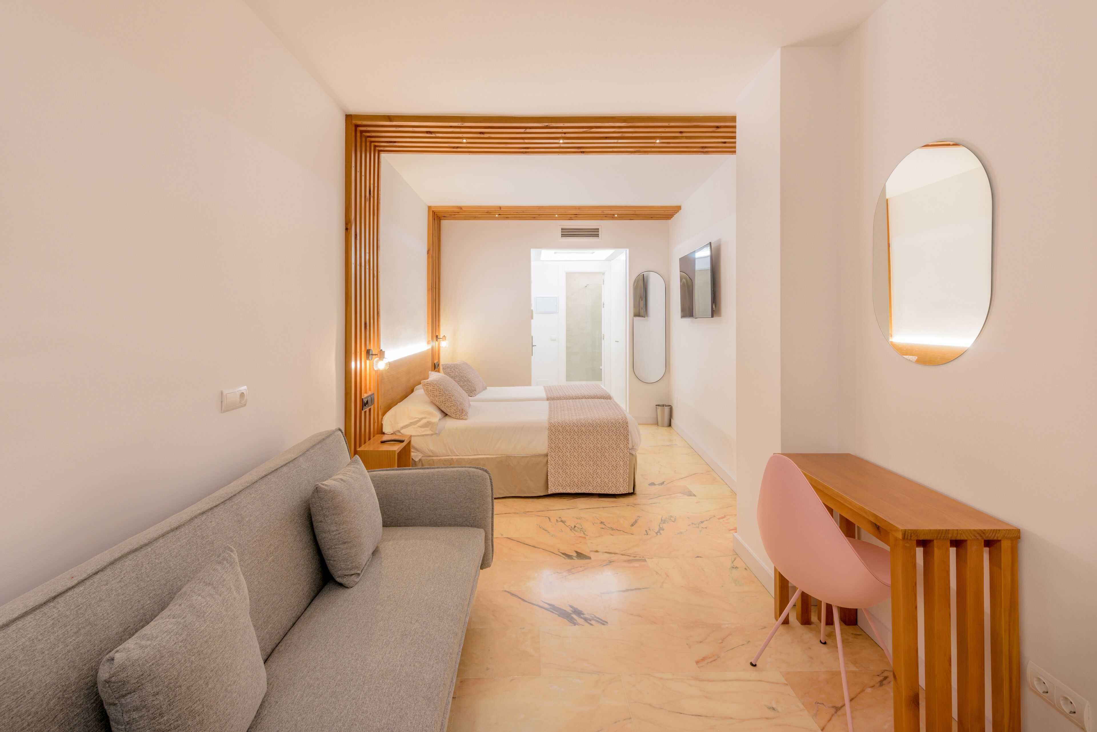 A modern hotel room with a sofa, a desk, and a bed.