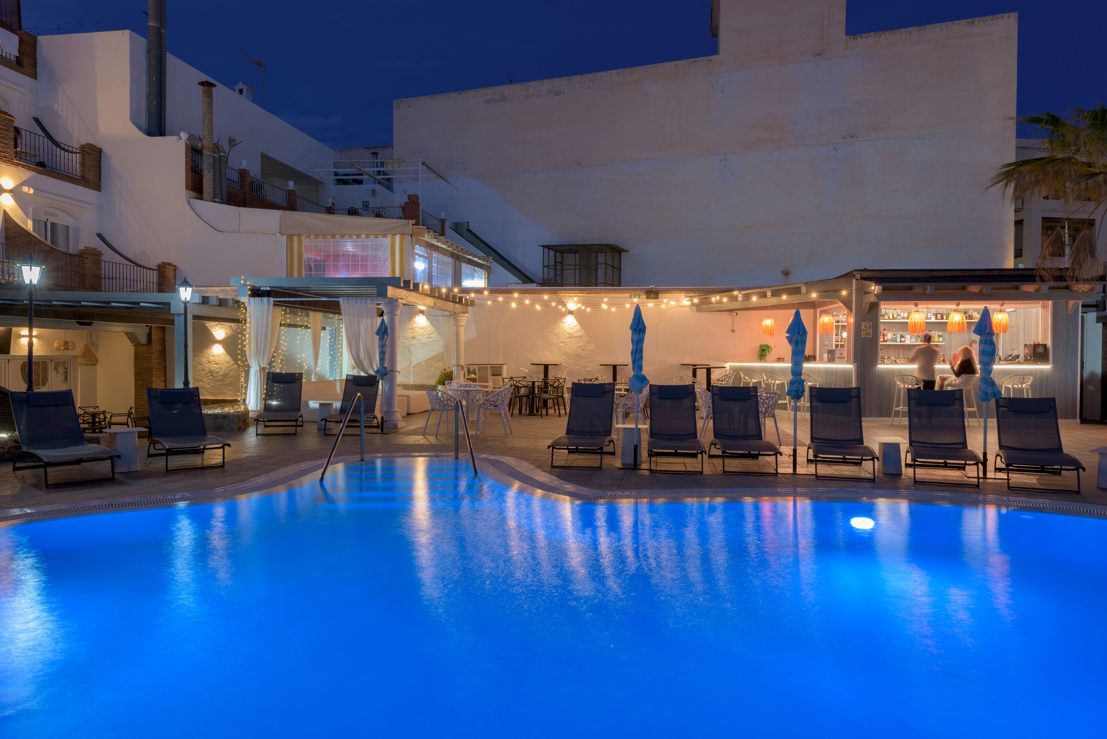 Un espace piscine avec des chaises longues et un bar.