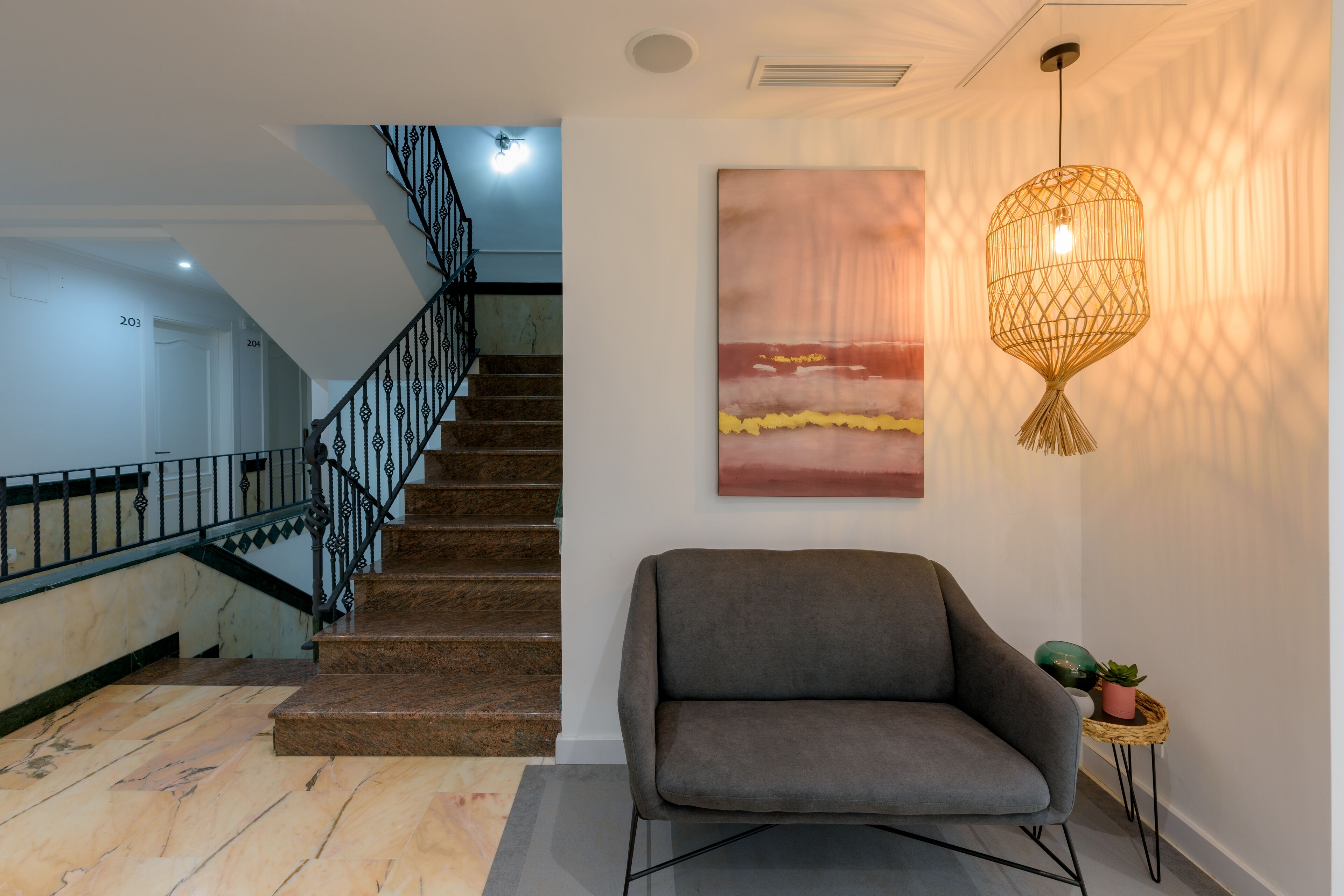 Una escalera con barandilla de metal, un sofá gris y una obra de arte colgada en la pared.