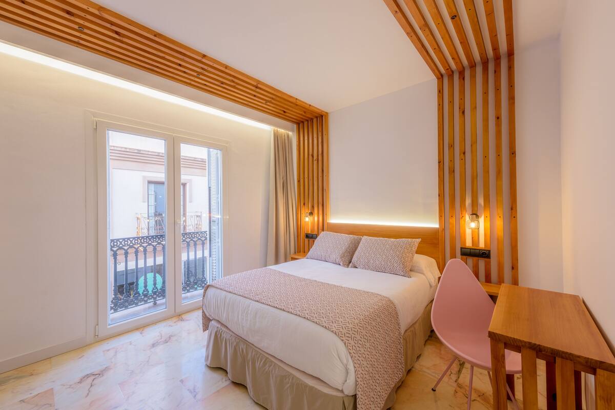Une chambre d’hôtel avec un lit, un plafond en bois, un balcon avec une balustrade et une table avec une chaise.