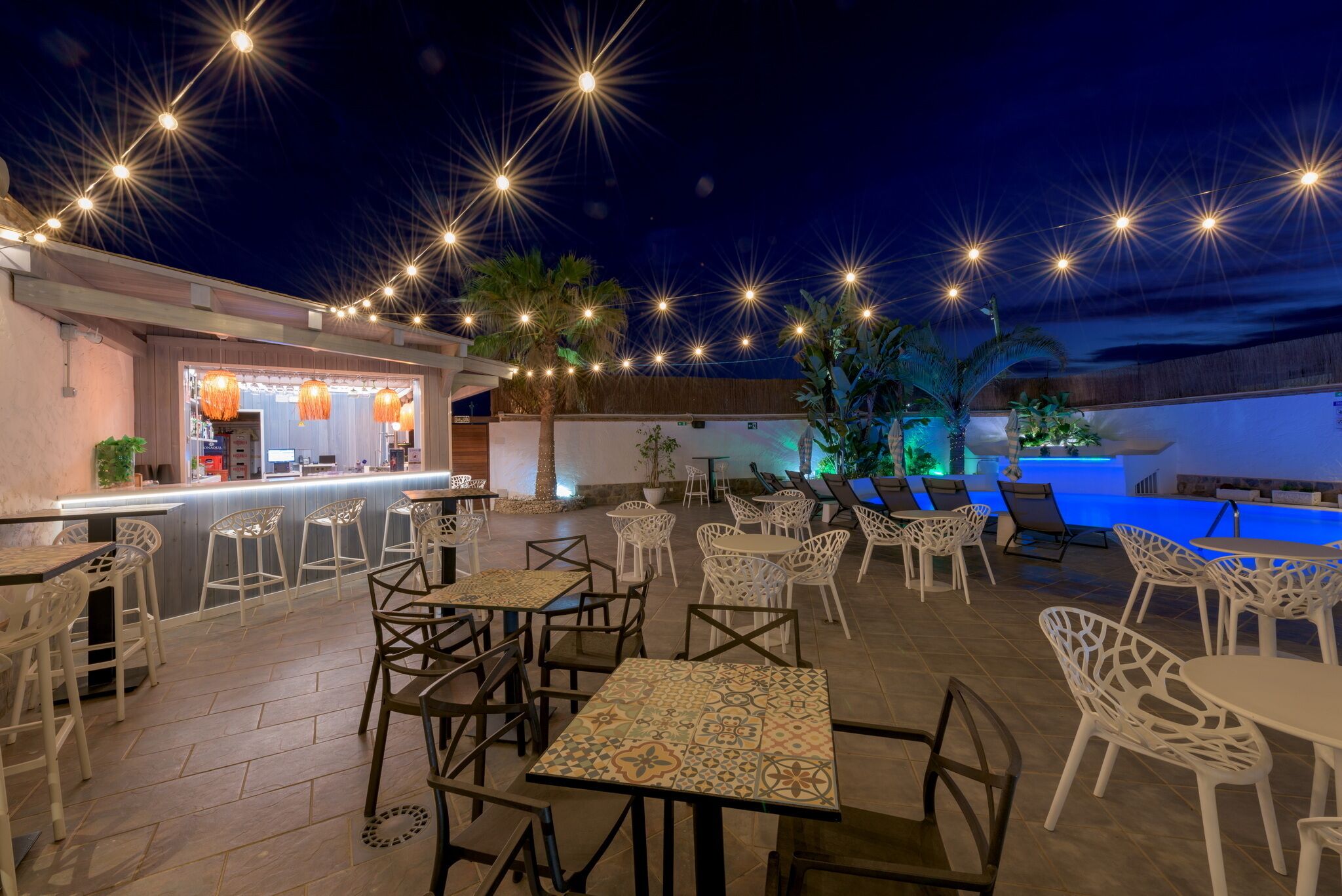 Un patio al aire libre con mesas y sillas, una zona de bar y una piscina.