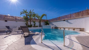 Une piscine bordée de chaises longues, avec un ciel bleu dégagé et un palmier.