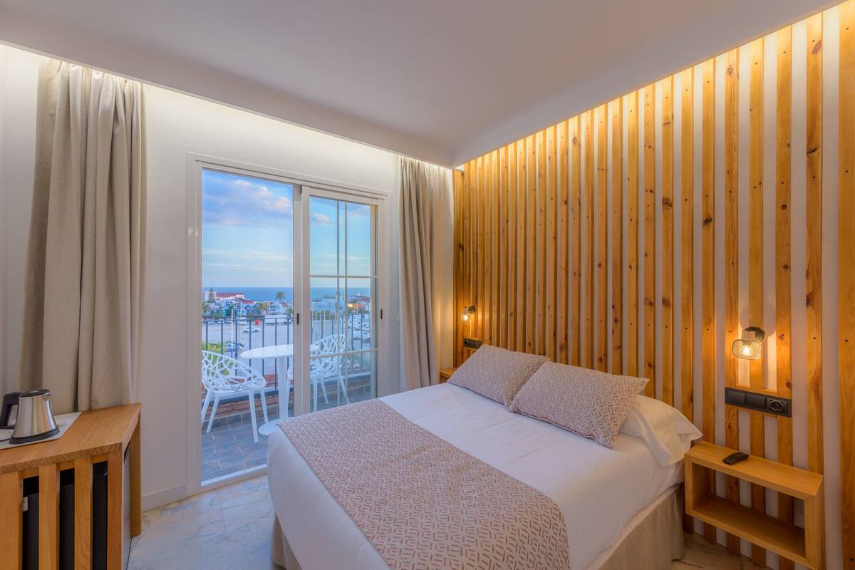 Une chambre avec un grand lit, un mur en bois, un balcon avec vue et une petite table avec une bouilloire.