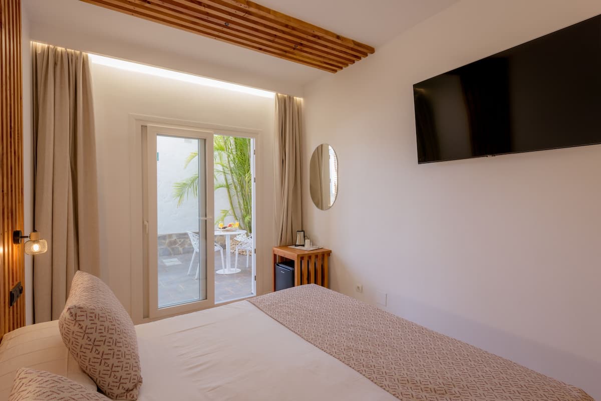 Une chambre d’hôtel avec un lit, une télévision, un plafond en bois, une porte-fenêtre coulissante et une petite table avec une lampe.