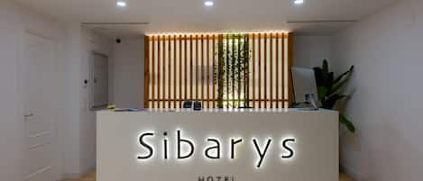 A hotel reception desk with a modern design, featuring a nameplate that reads "Sibarys HOTEL."