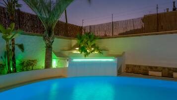 Una piscina con un muro blanco y una valla de madera al fondo.