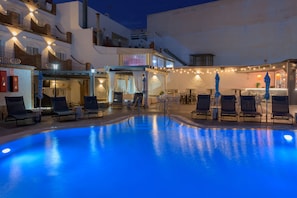 A swimming pool with lounge chairs and umbrellas, surrounded by buildings with balconies and string lights. - Sibarys Hotel Boutique (Nerja)