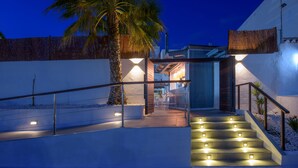 A modern building with a staircase leading to a covered entrance, palm tree, and outdoor seating area.