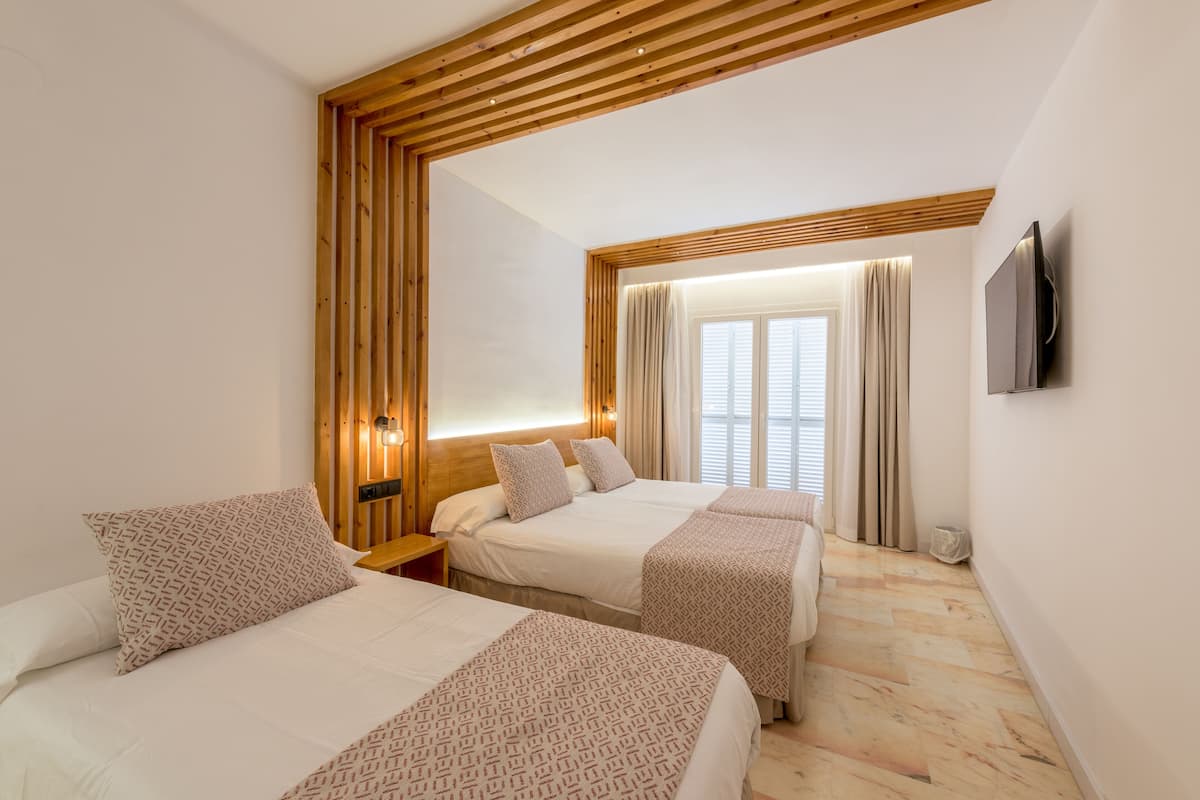Une chambre d’hôtel avec deux lits, des poutres en bois au plafond, un téléviseur fixé au mur et une fenêtre avec des rideaux.