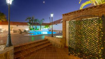 A pool area with steps leading to a covered patio, a brick wall, and a decorative lattice with lights.