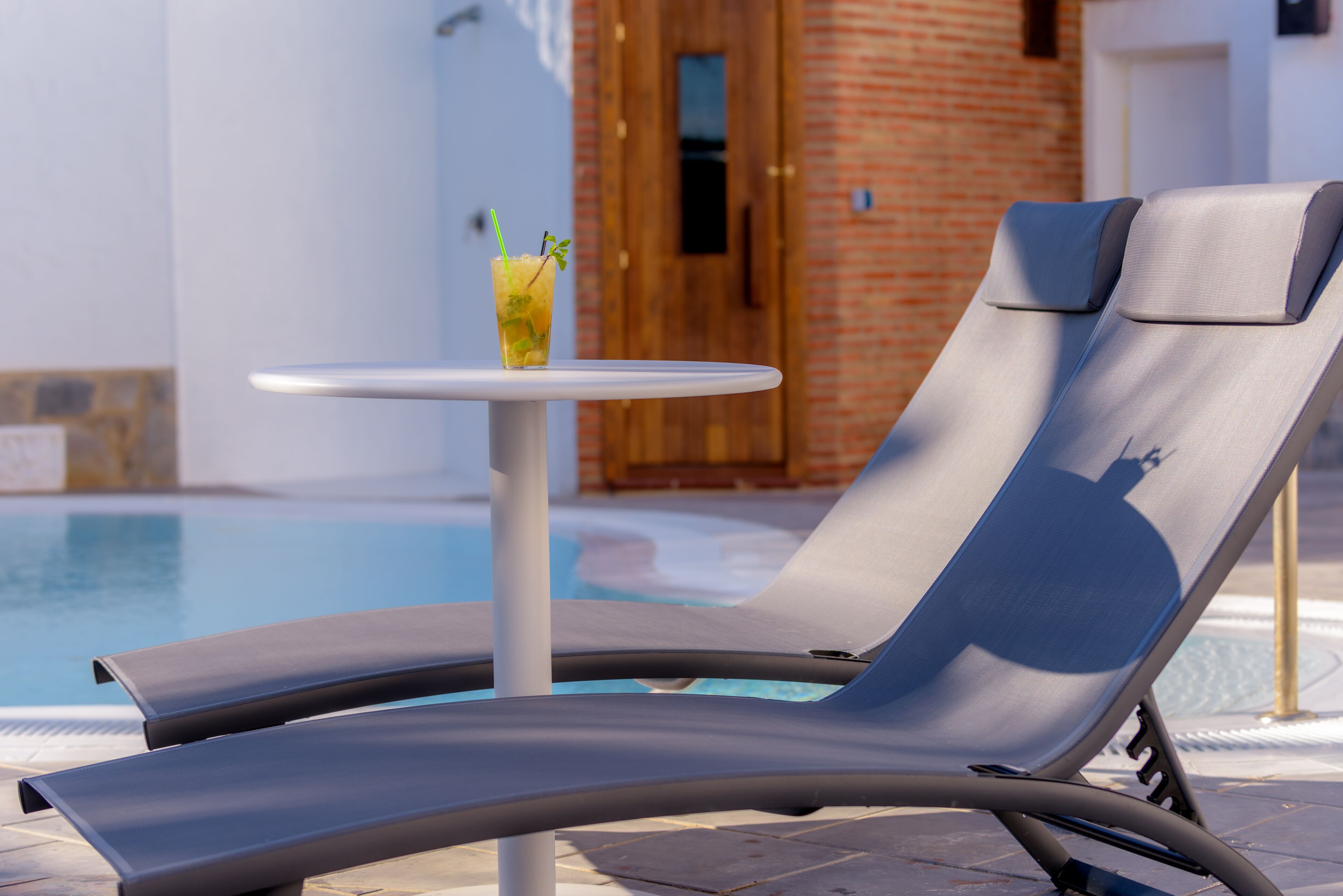 A poolside lounge chair with a small table and a drink.