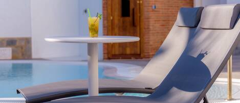A poolside lounge chair with a small table and a drink.