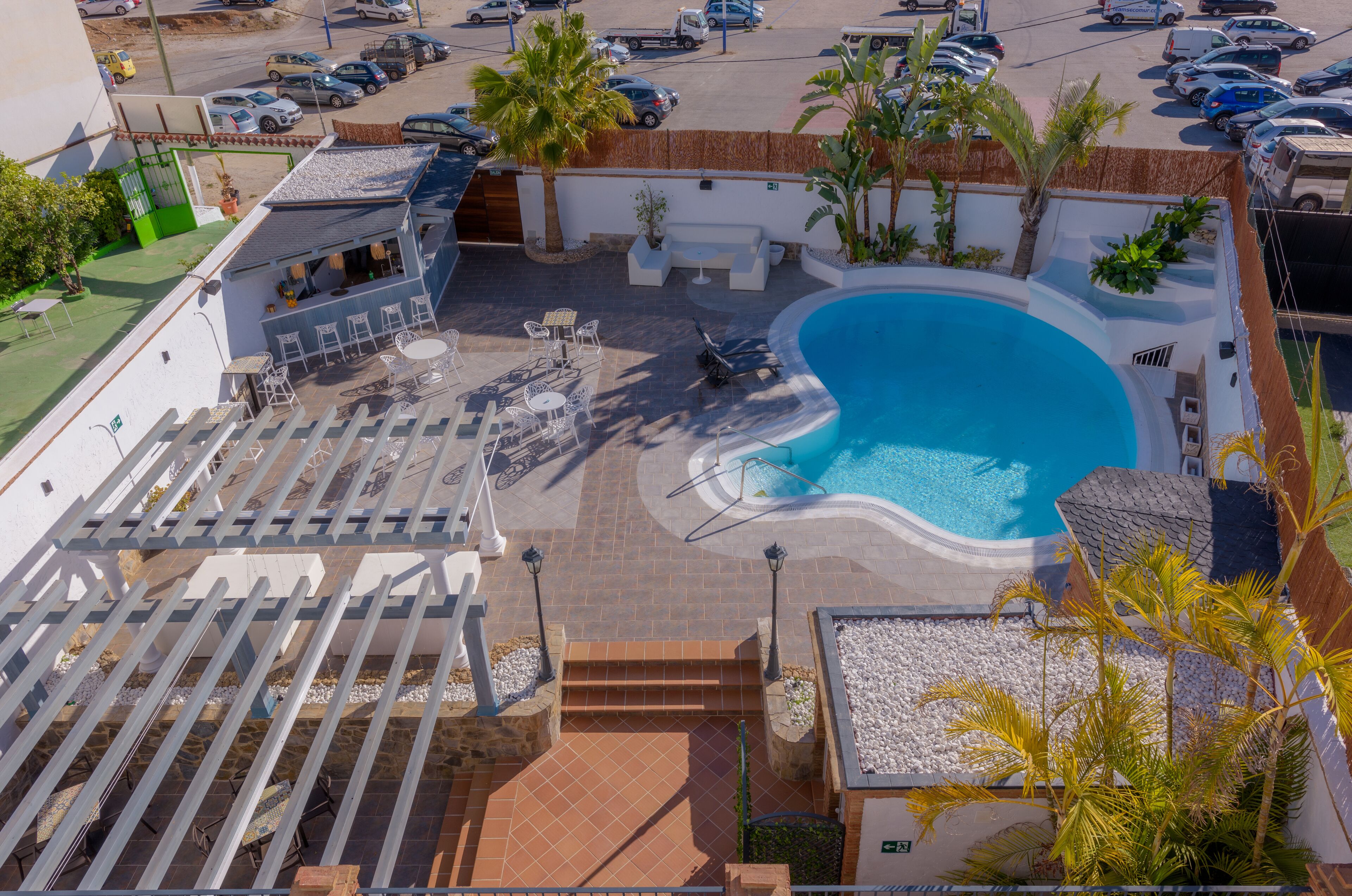 A rooftop pool area with a seating area, palm trees, and a view of the parking lot.