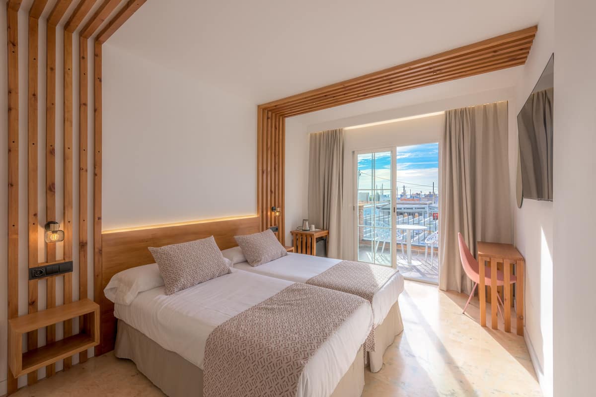Une chambre d’hôtel moderne avec deux lits, un plafond en bois, un balcon avec vue et une petite table avec une chaise.