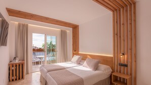 A modern hotel room with two beds, a wooden headboard, a small bedside table, and a view of the outdoor area.