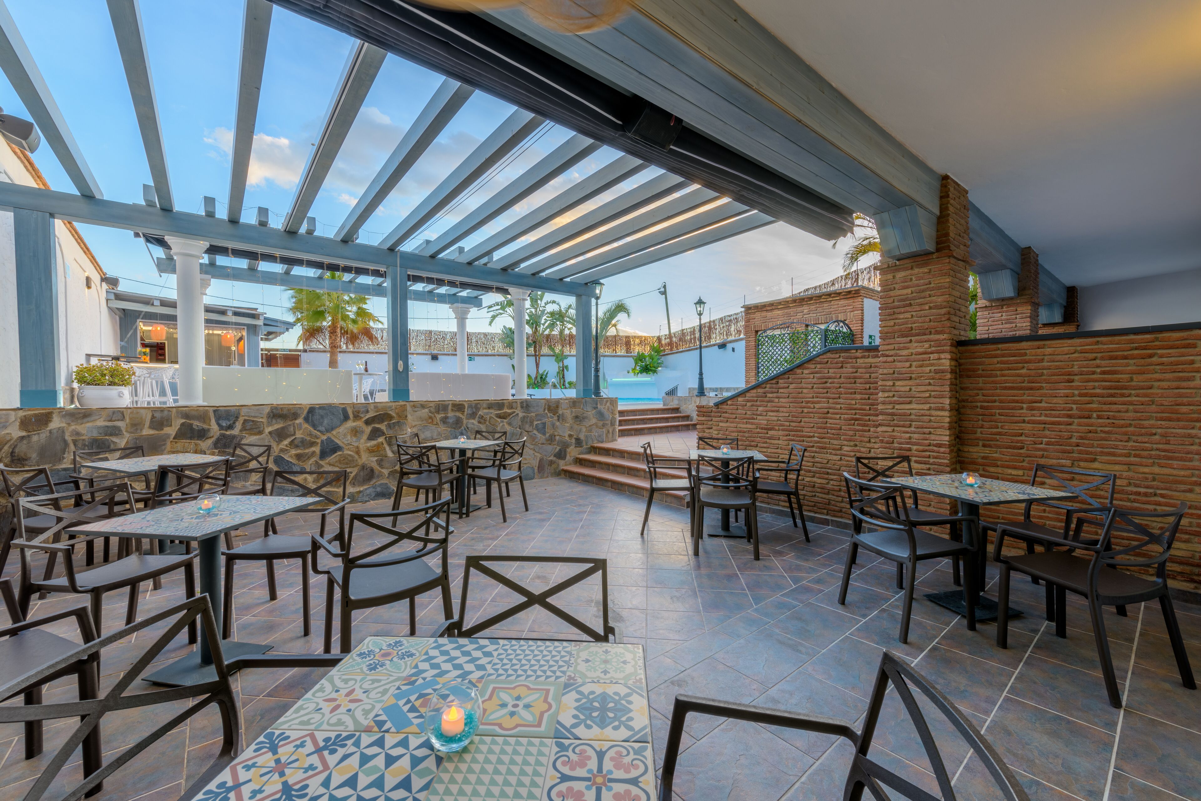 Un patio al aire libre con mesas y sillas, un muro de piedra y vistas a una piscina.