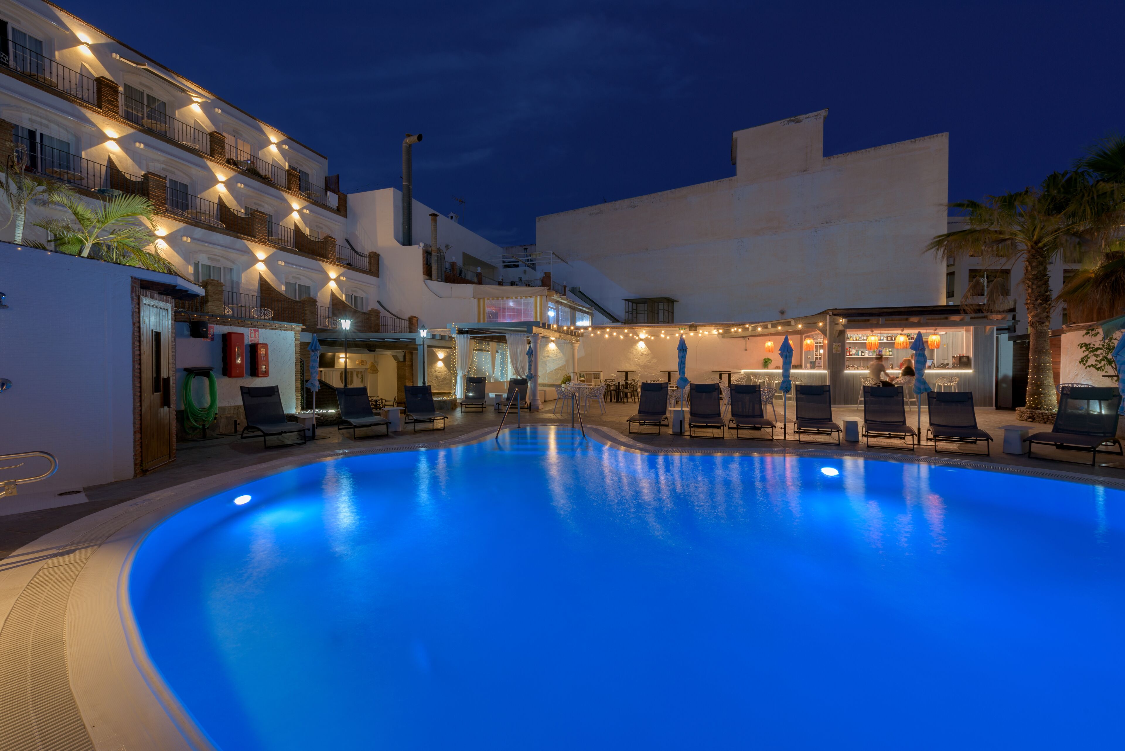 A swimming pool with lounge chairs, a bar area, and a building with balconies.