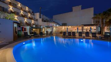 A swimming pool with lounge chairs, a bar area, and a building with balconies.