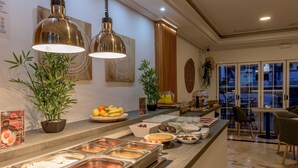 A buffet area with various food options, including fruits, vegetables, and meats, and a seating area with chairs and a table.