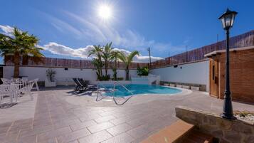 Une piscine baignée de soleil, un patio couvert avec des chaises et un lampadaire.