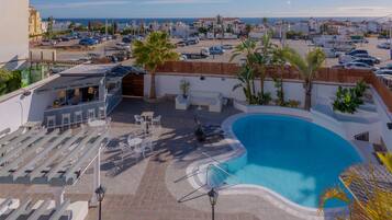 A rooftop pool area with a view of the sea, outdoor seating, and a parking lot.
