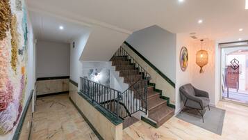 A spacious hallway with a marble floor, a staircase with a metal railing, and a chair near a glass door.