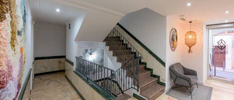 A spacious hallway with a marble floor, a staircase with a metal railing, and a chair near a glass door.