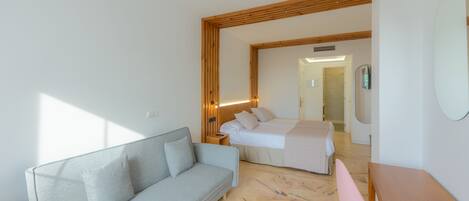 A modern hotel room with a sofa, a bed, a wooden table, and a chair.