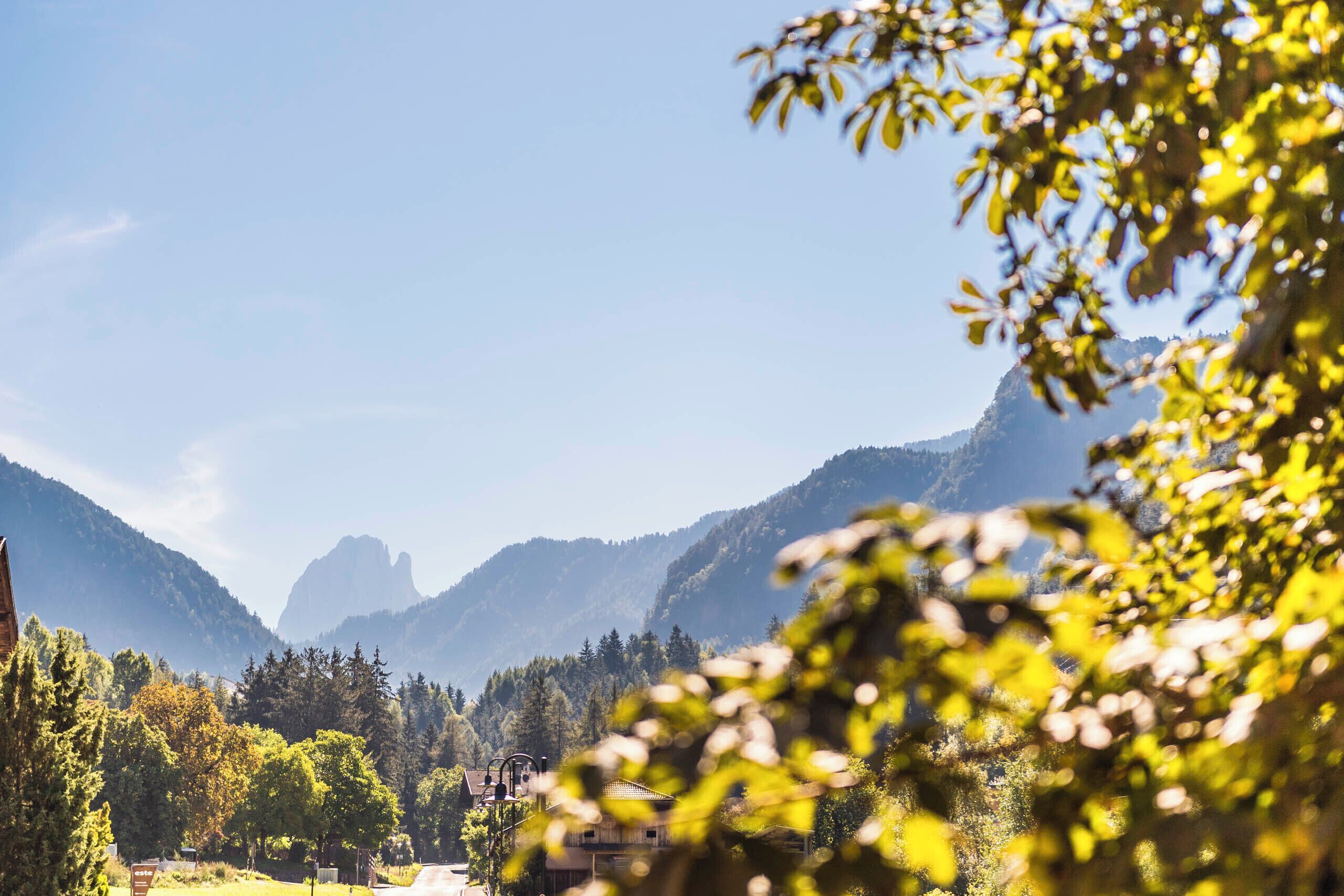 A mountain landscape with a clear sky, a road, and buildings in the valley.