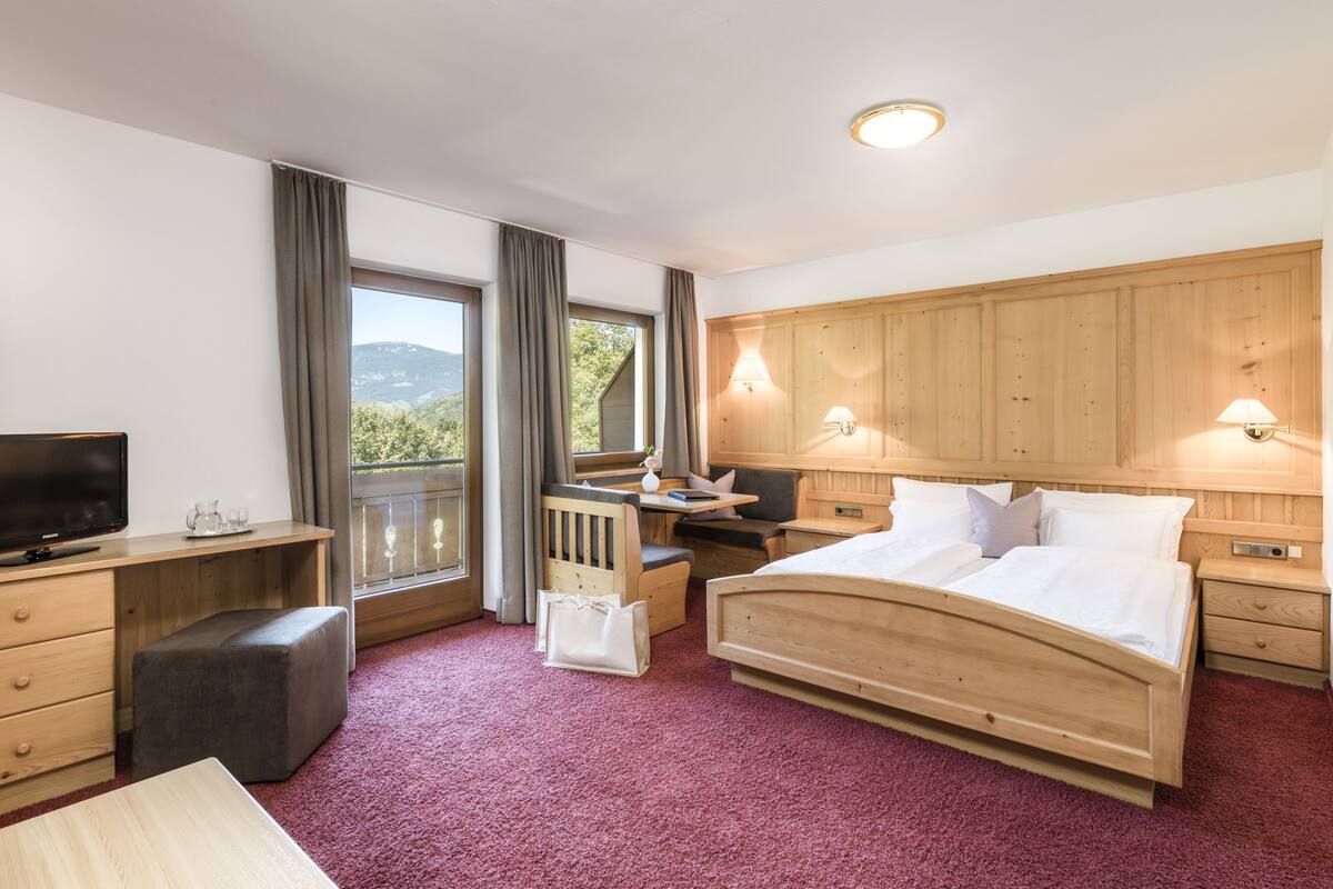 A hotel room with a bed, a desk, a television, and a window with curtains.