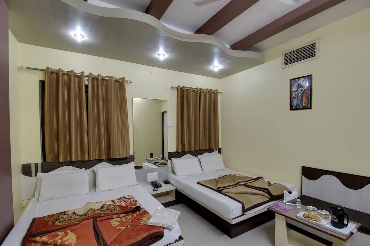 A hotel room with two beds, a bedside table with a kettle and snacks, a mirror, and a painting on the wall.