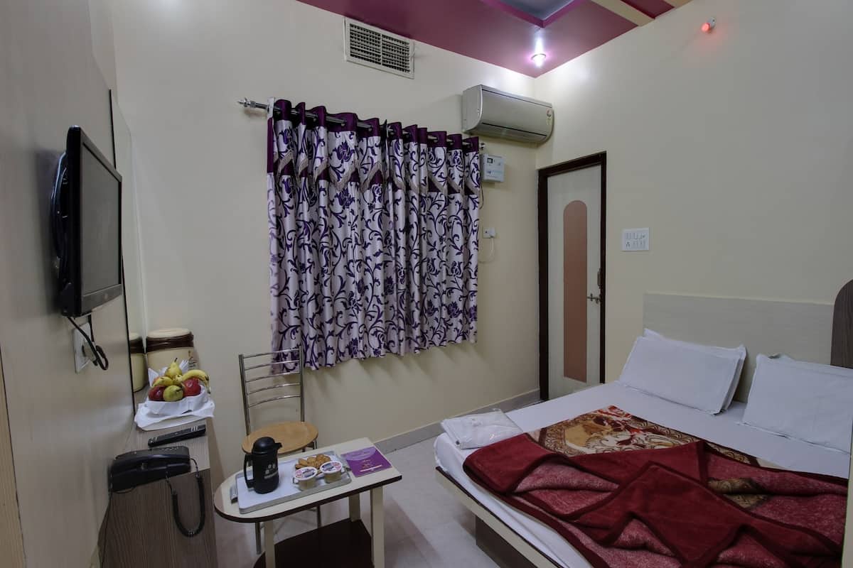 A hotel room with a bed, a small table with a coffee maker, a fruit bowl, and a television on the wall.