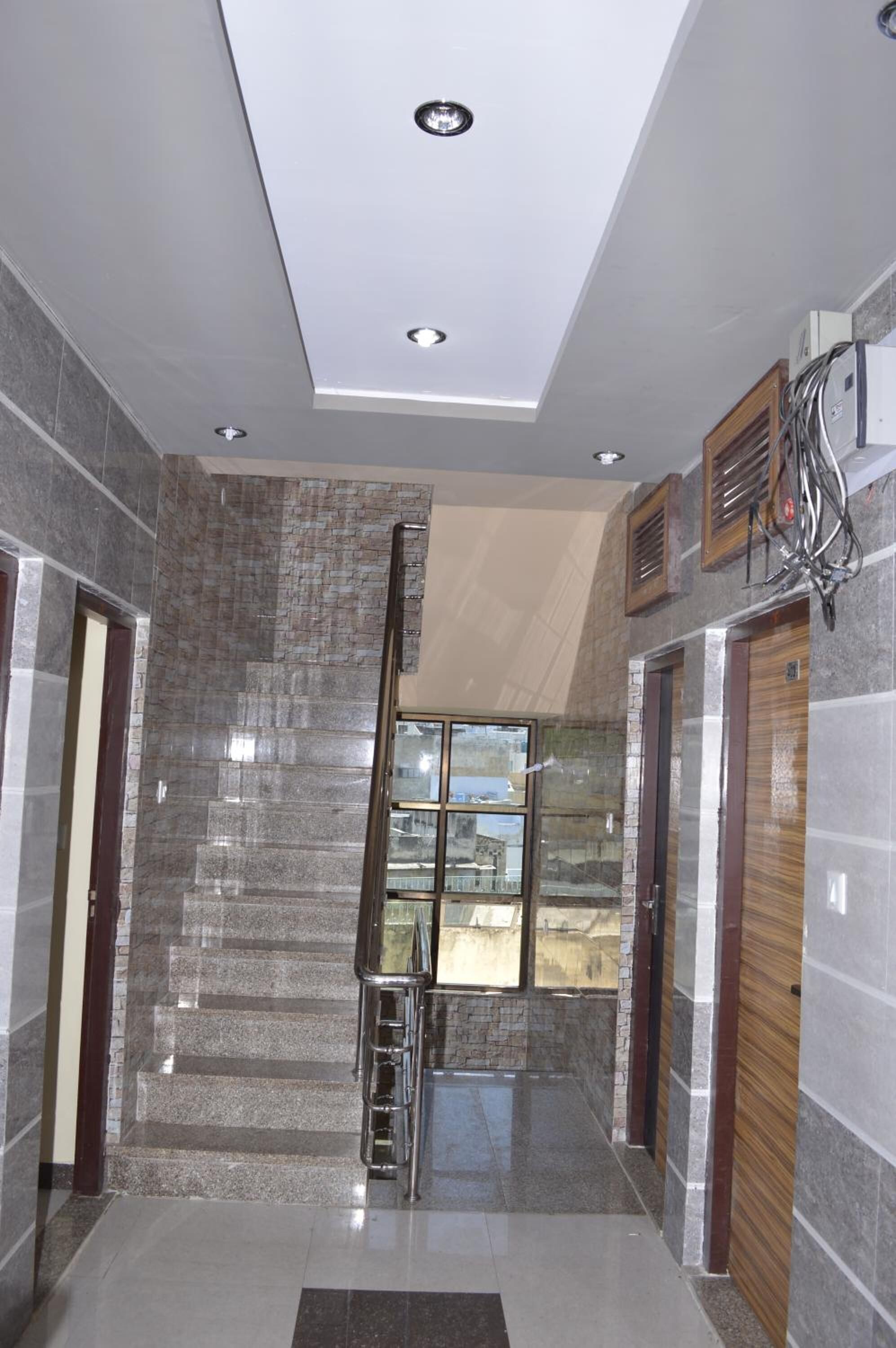 A modern hallway with a glass elevator shaft, a large window, and a polished stone wall.