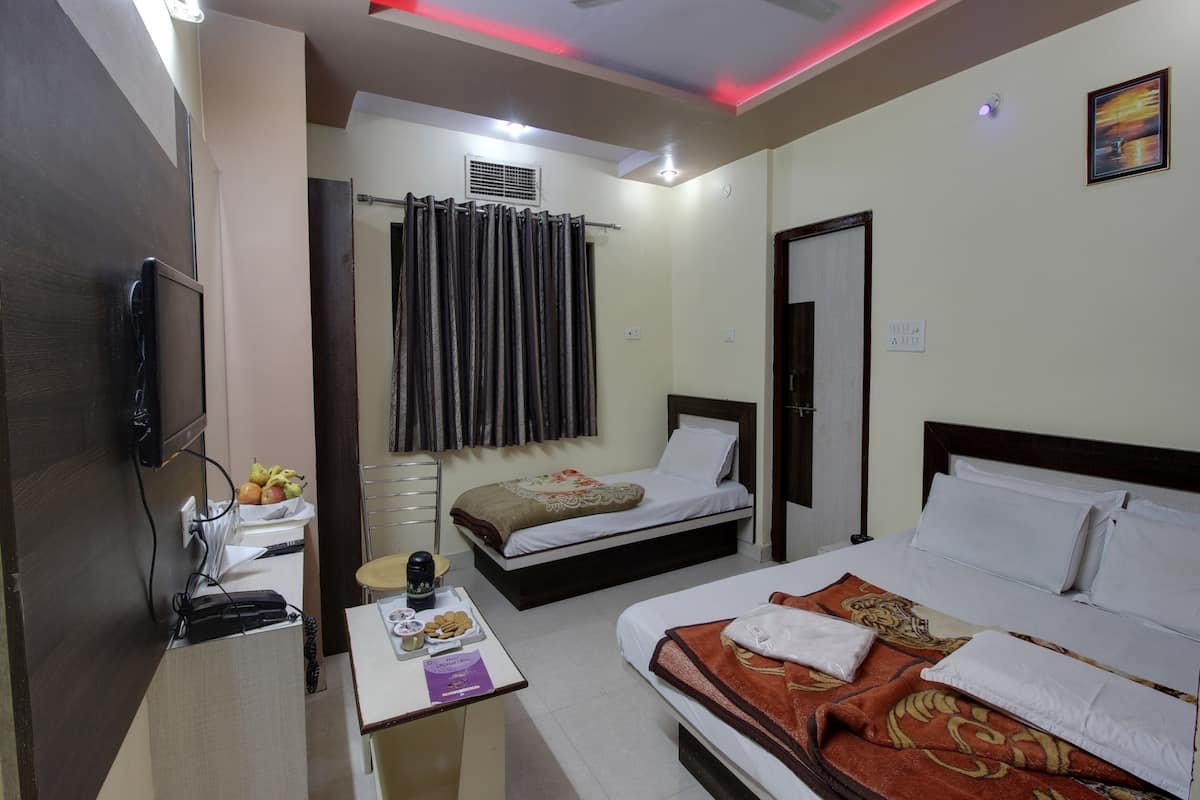 A hotel room with two beds, a desk with a computer and a lamp, a ceiling fan, and a window with curtains.