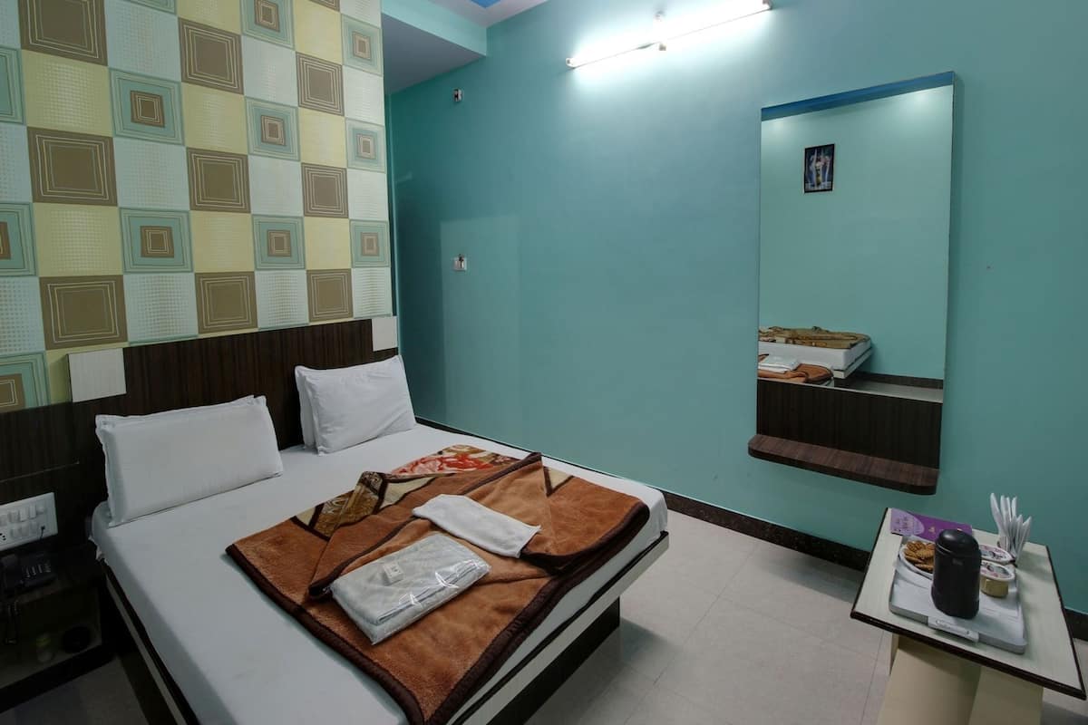 A hotel room with a bed, a bedside table with a phone and a coffee maker, a wall with a geometric pattern, and a mirror.