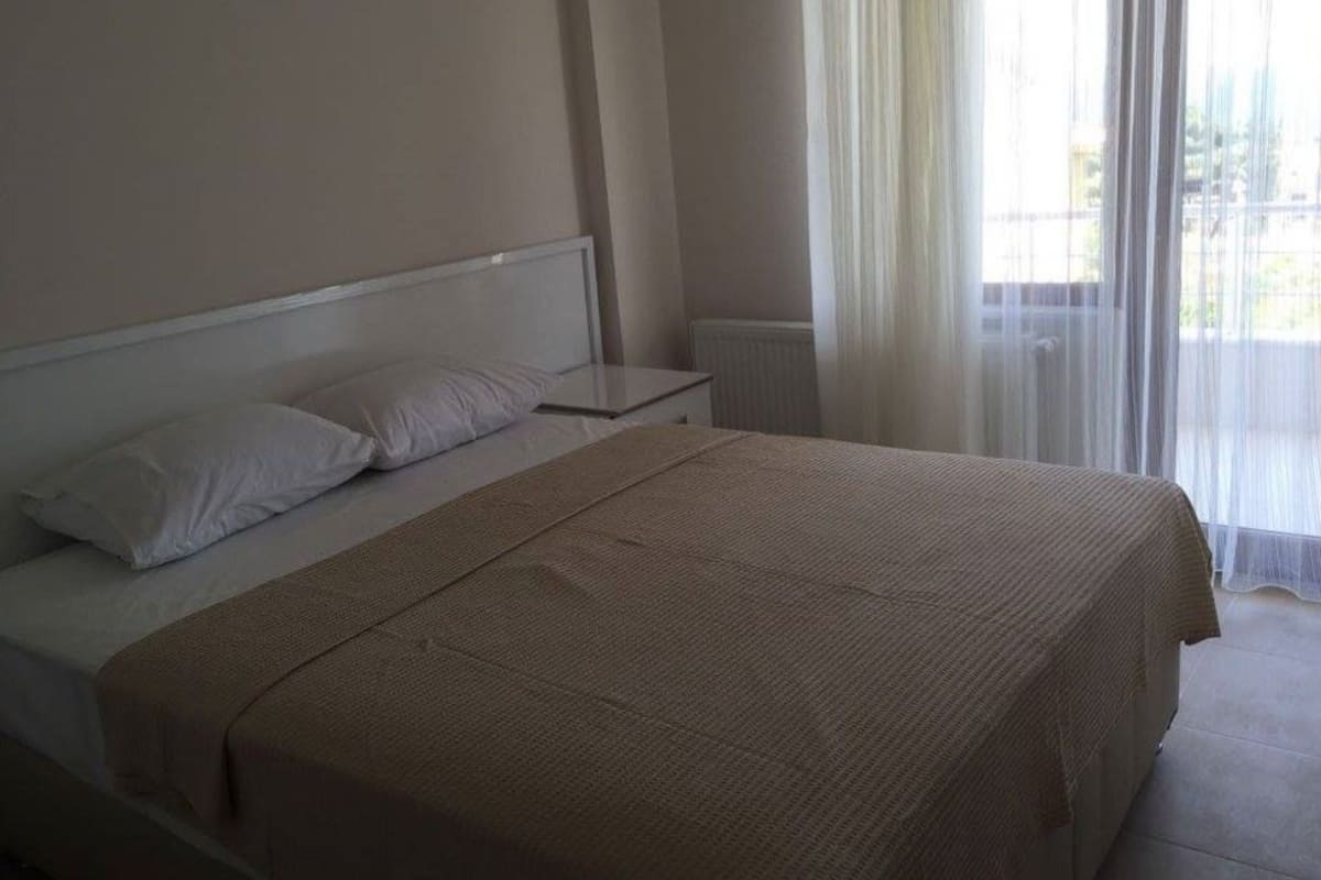 Un dormitorio con cama, mesita de noche y ventana con cortinas ligeras.