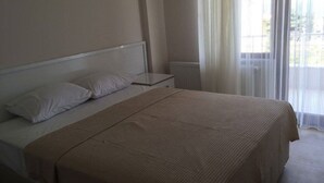 A bedroom with a bed, a nightstand, and a window with sheer curtains.